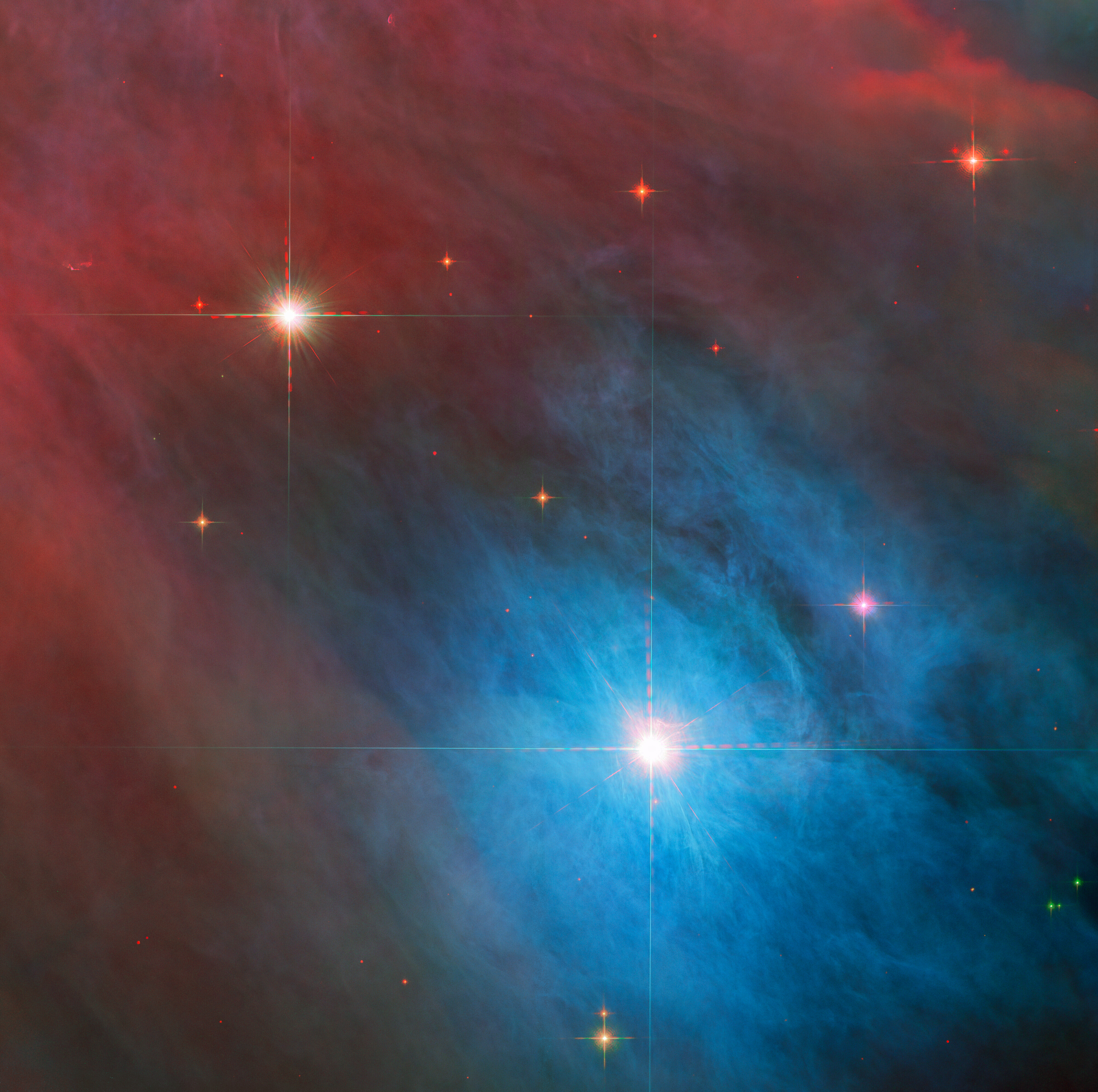 Two stars with diffraction spikes shine brightly in the image. The larger star, at lower right, is in a bright blue cloud of gas and dust, while the smaller star at upper left is in a red haze. The clouds are somewhat patchy. Smaller red stars are scattered around them.