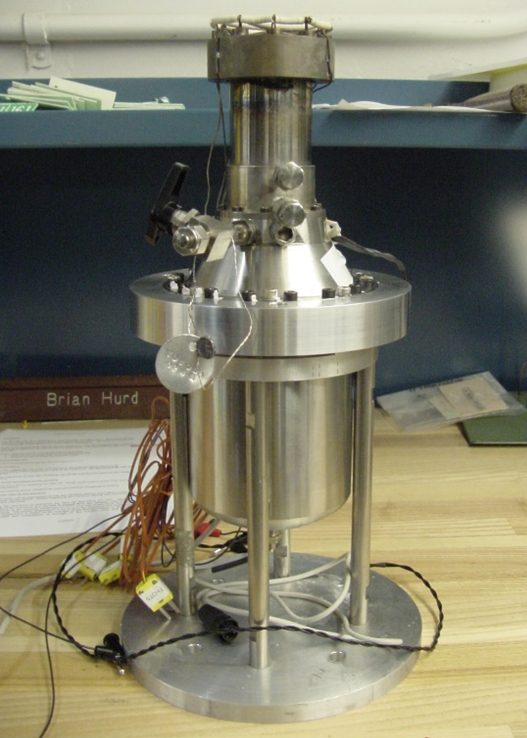 Metallic 55-watt Stirling convertor with cylindrical housing, wiring, and vertical mounting for long-duration space power testing.
