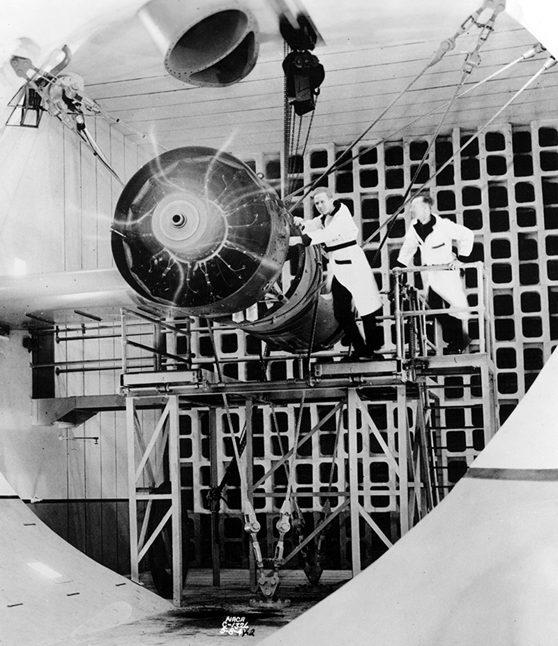 Two men with large aircraft engine in test cell.