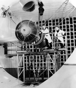 Two men with large aircraft engine in test cell.