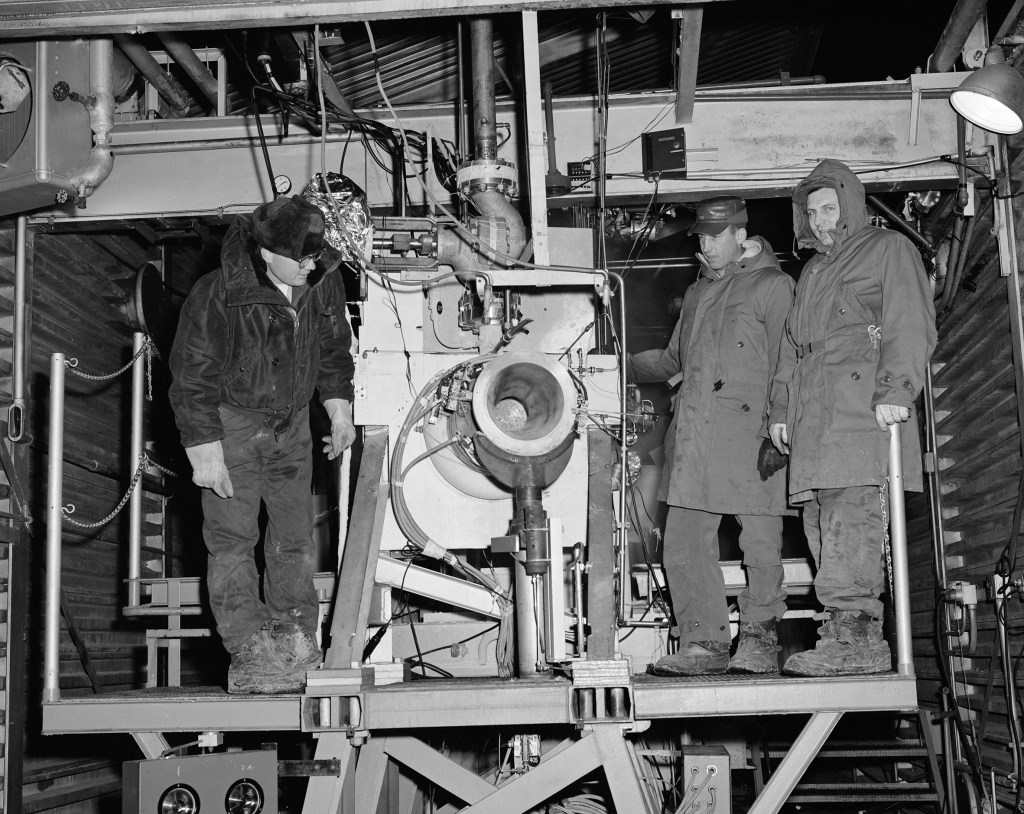 Three men on with rocket engine on platform in J-1