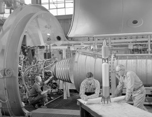 Men looking at rocket model with engine in the background.
