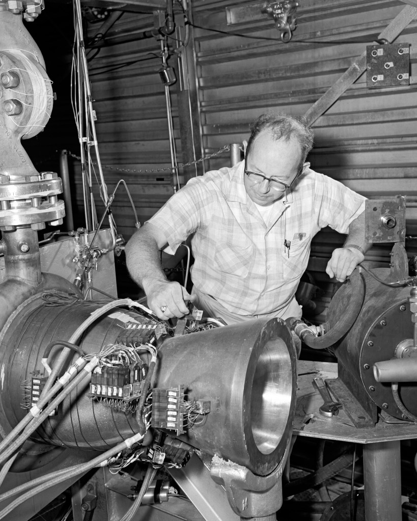 A technician inspects an experimental copper nozzle at the J-1 test rig