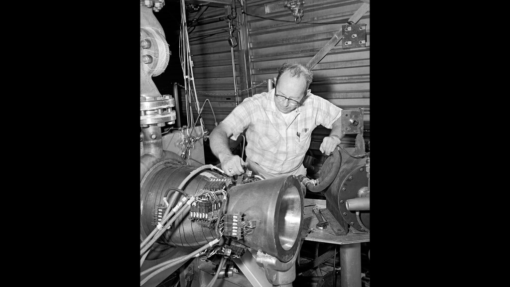 A technician inspects an experimental copper nozzle at the J-1 test rig