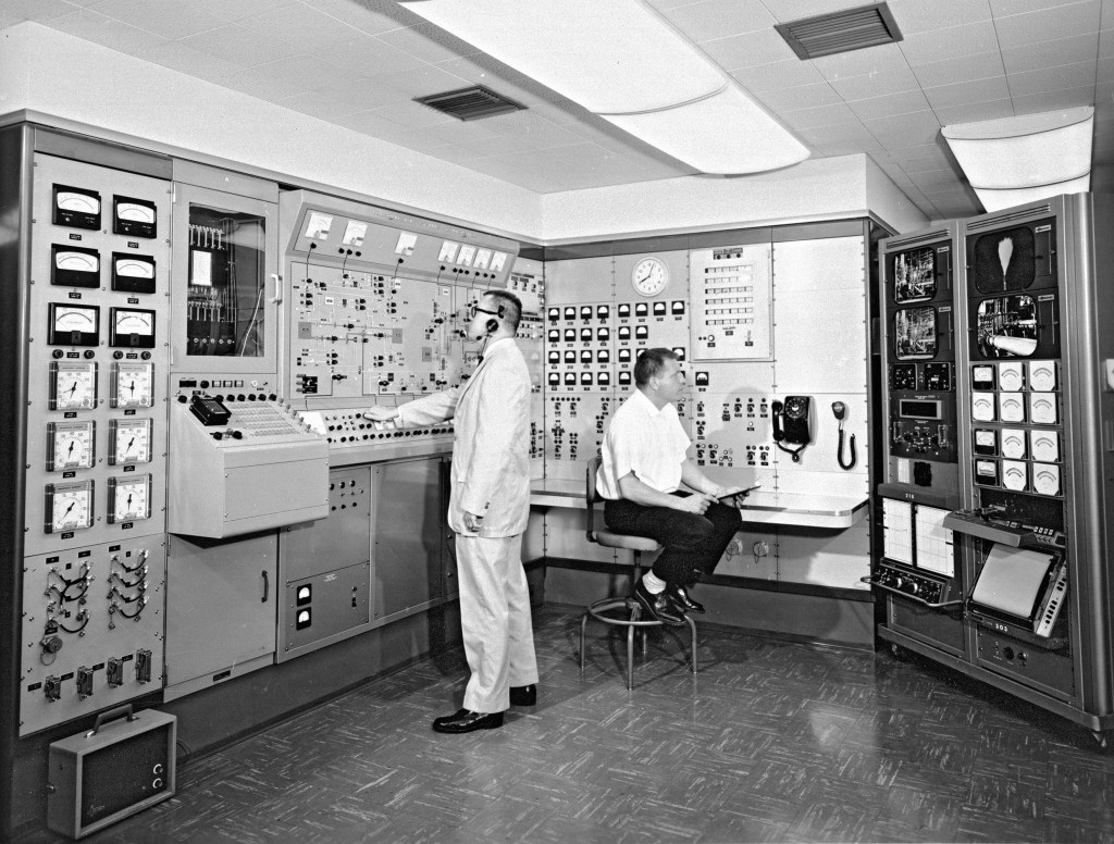 Two men at control panels in H Control Building