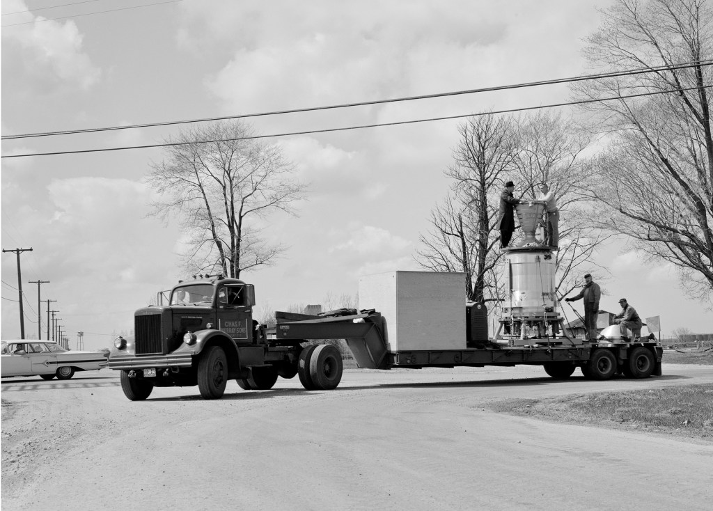Truck pulls trailer bed with Kiwi engine on it.