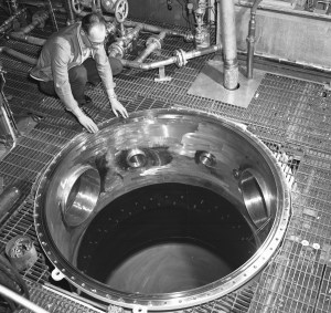 Two technicians working on calorimeter suspended by crane.