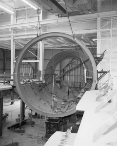 Large tubular hardware lowered by crane.