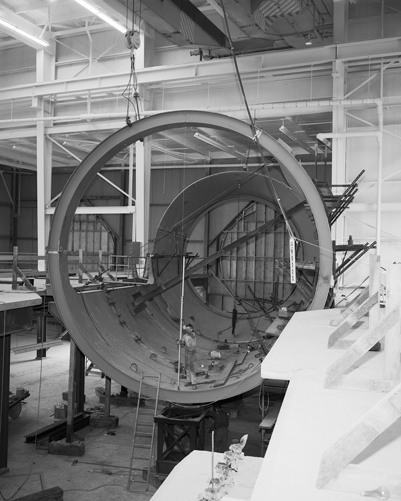 Large tubular hardware lowered by crane.