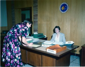 Woman at desk and another signing logbook.
