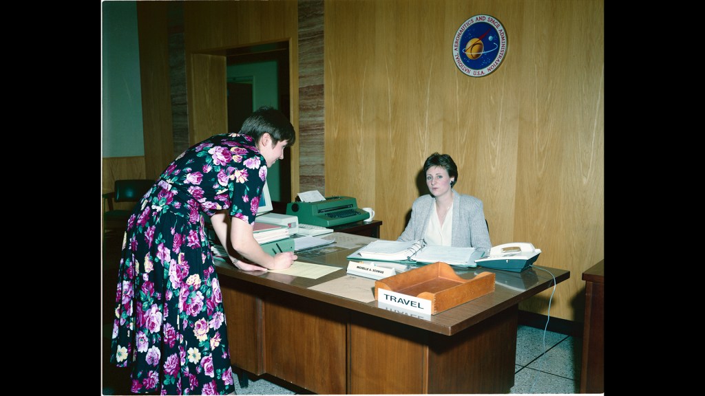 Woman at desk and another signing logbook.