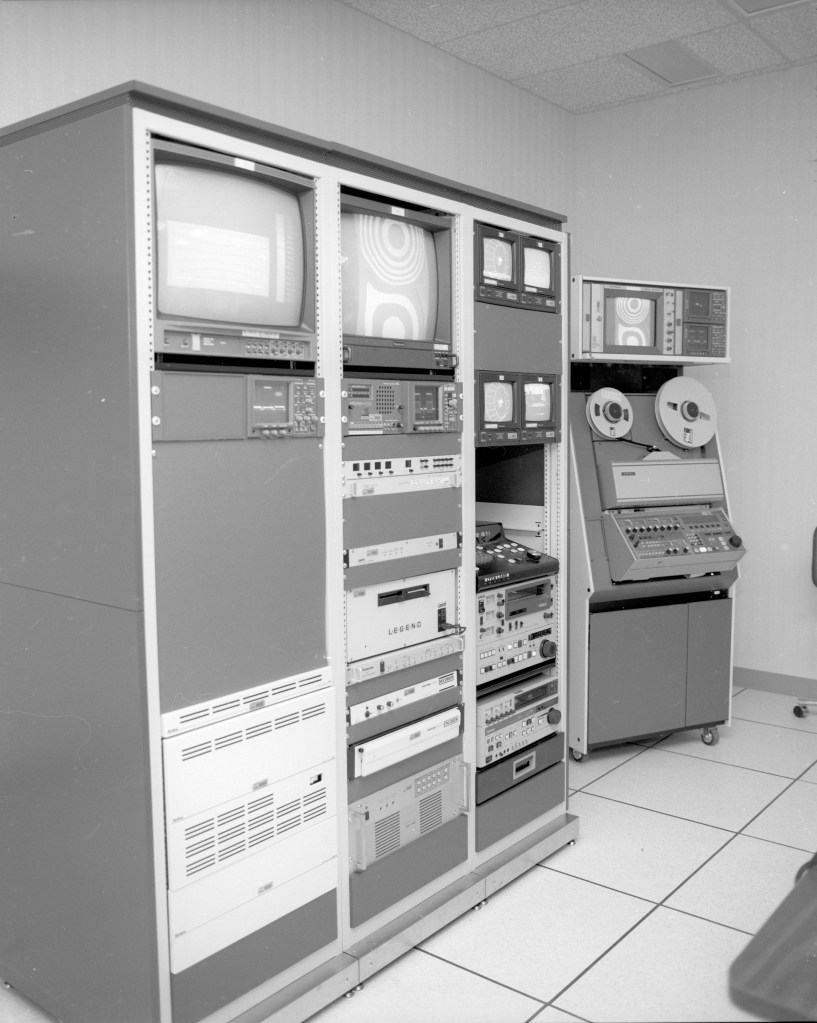 A large, rectangular technological device covered with large screens and tiny buttons sits in an empty room.