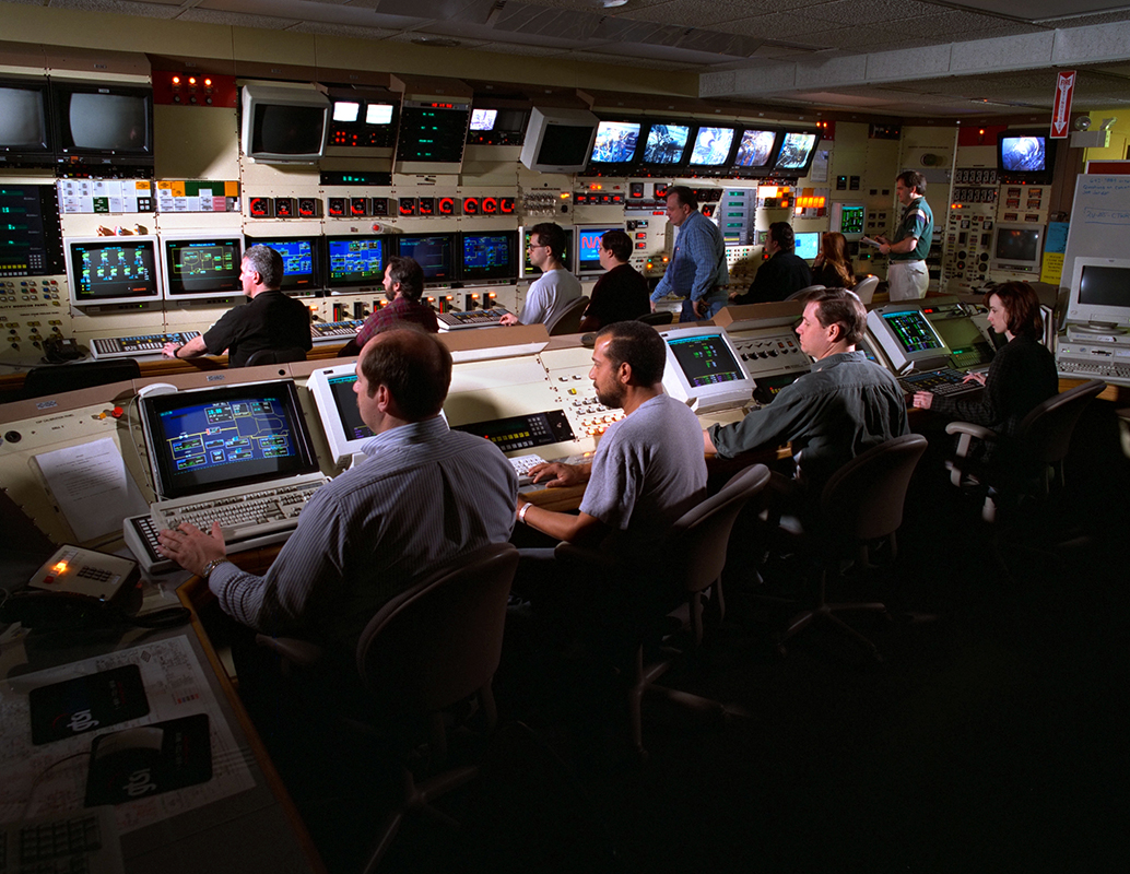 Engineers at consoles in control room.