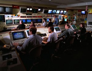 Engineers at consoles in control room.