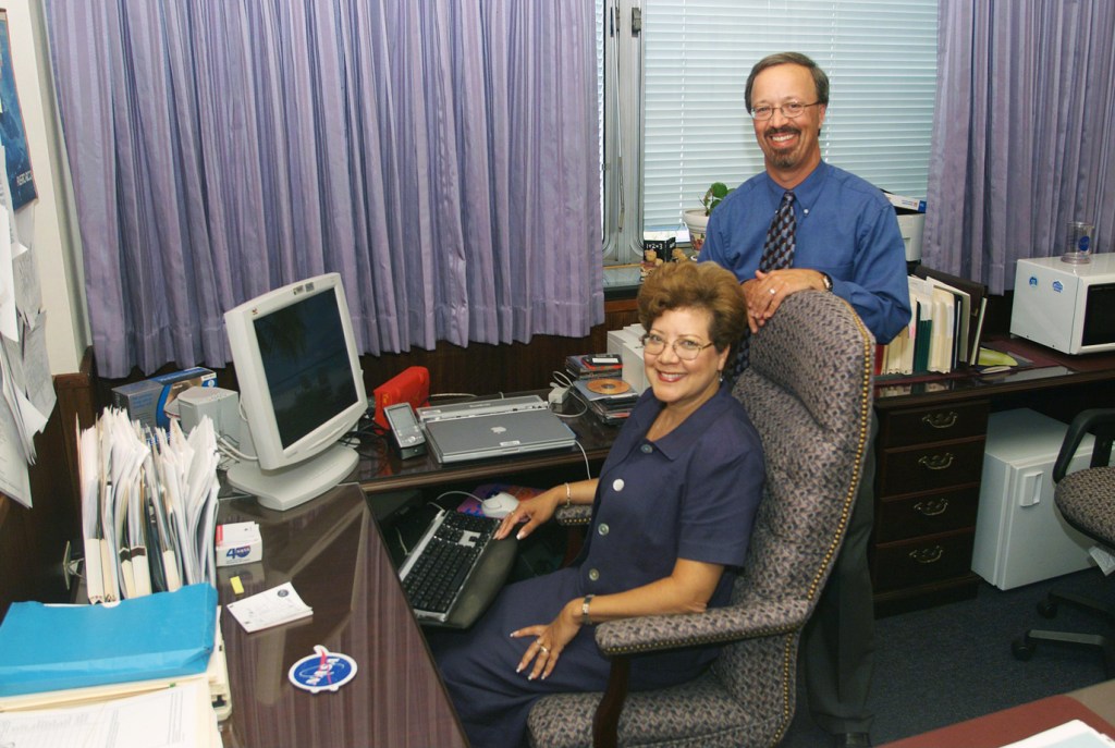 Woman at desk and man standing.