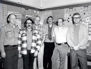 Group of men standing in control room.