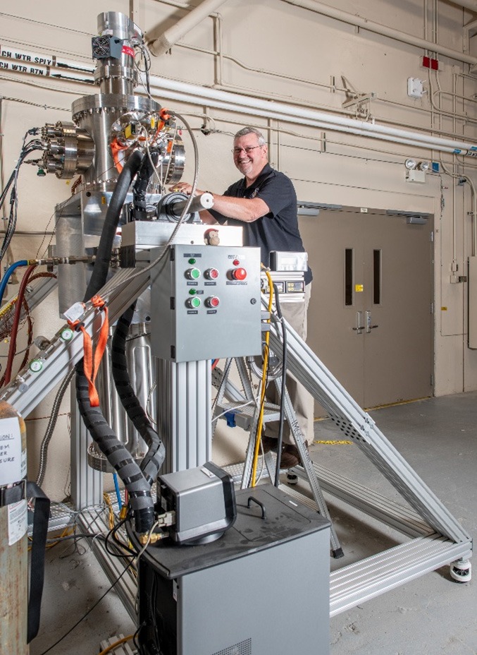 Engineer adjusts equipment for a sodium heat pipe test inside a large metal vacuum chamber with control panels and insulated wiring.