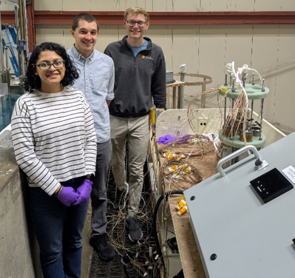 NASA engineers and a graduate student stand beside reactor equipment and thermocouples, preparing for heat pipe tests in a high-bay lab environment.