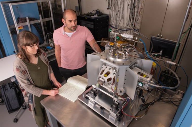 Two NASA engineers test an electrically heated Stirling generator in a lab, collecting data from a table-mounted power system.