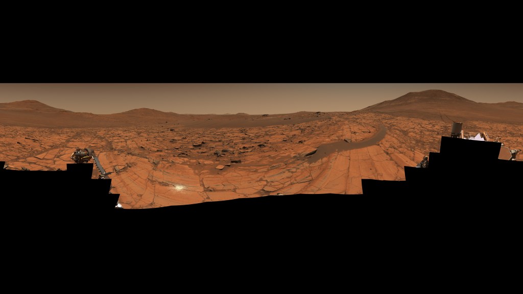 In this natural-color version of the “Falbreen” panorama, colors have not been en-hanced and the sky appears more reddish. Visible still is Perseverance’s 43rd rock abrasion (the white patch at center-left). The 96 images stitched together to create this 360-degree view were acquired May 26, 2025.