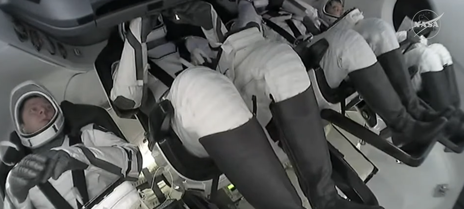 image shows four people in white and black suits inside a spacecraft.