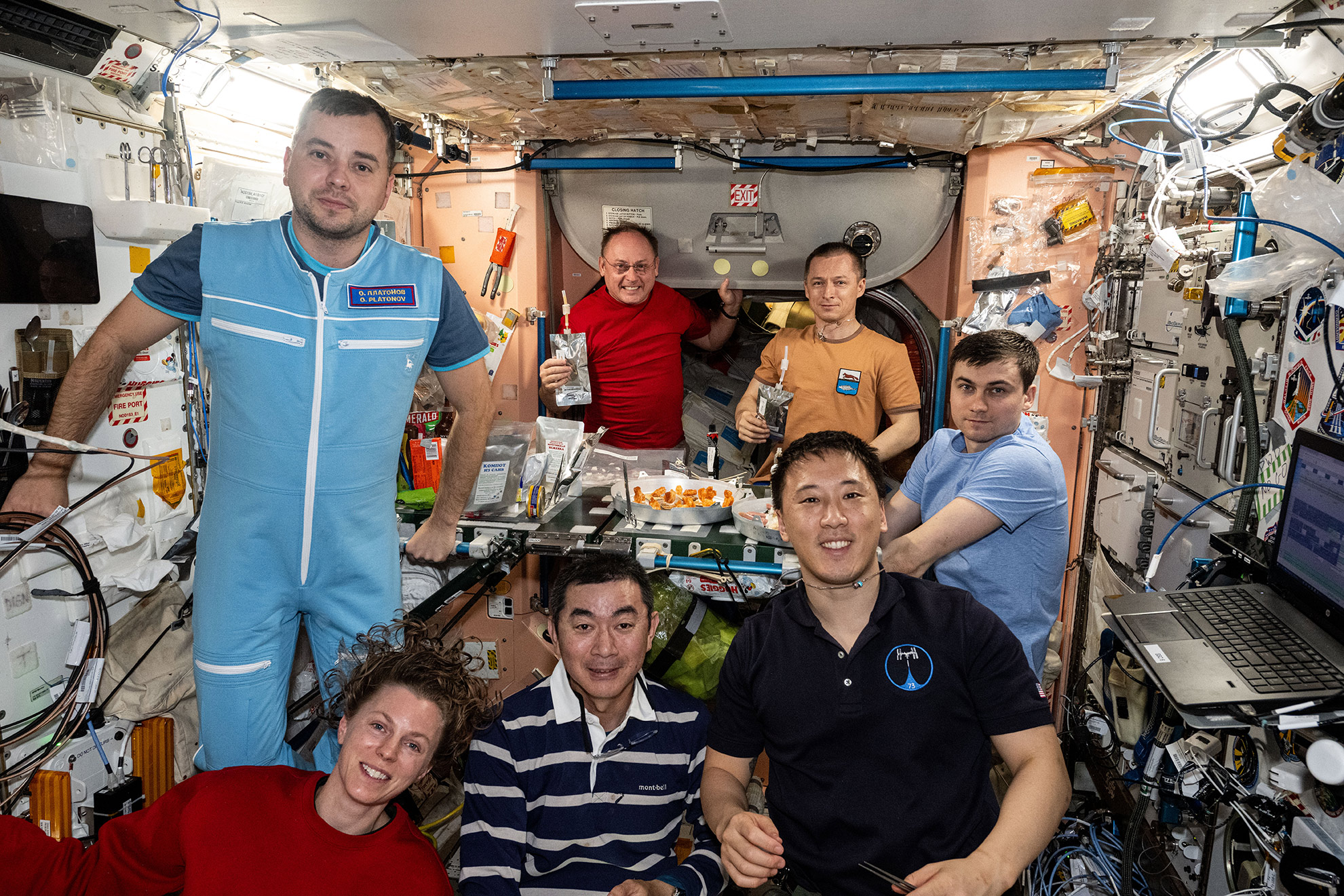 The seven-member Expedition 73 crew gathers together for a dinnertime portrait inside the galley of the International Space Station's Unity module. In the front from left are, Flight Engineers Zena Cardman of NASA, Kimiya Yui of JAXA (Japan Aerospace Exploration Agency), and Jonny Kim of NASA. In the back are, Flight Engineers Oleg Platonov of Roscosmos and Mike Fincke of NASA, and station Commander Sergey Ryzhikov and Alexey Zubritsky, both from Roscosmos.