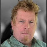 Headshot of a man with blonde hair and goatee, wearing a green collared shirt.