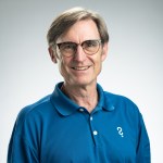 Headshot of a man with gray hair, wearing glasses and a blue polo shirt.