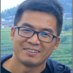 Headshot of a man with short black hair, black glasses, and a black shirt.
