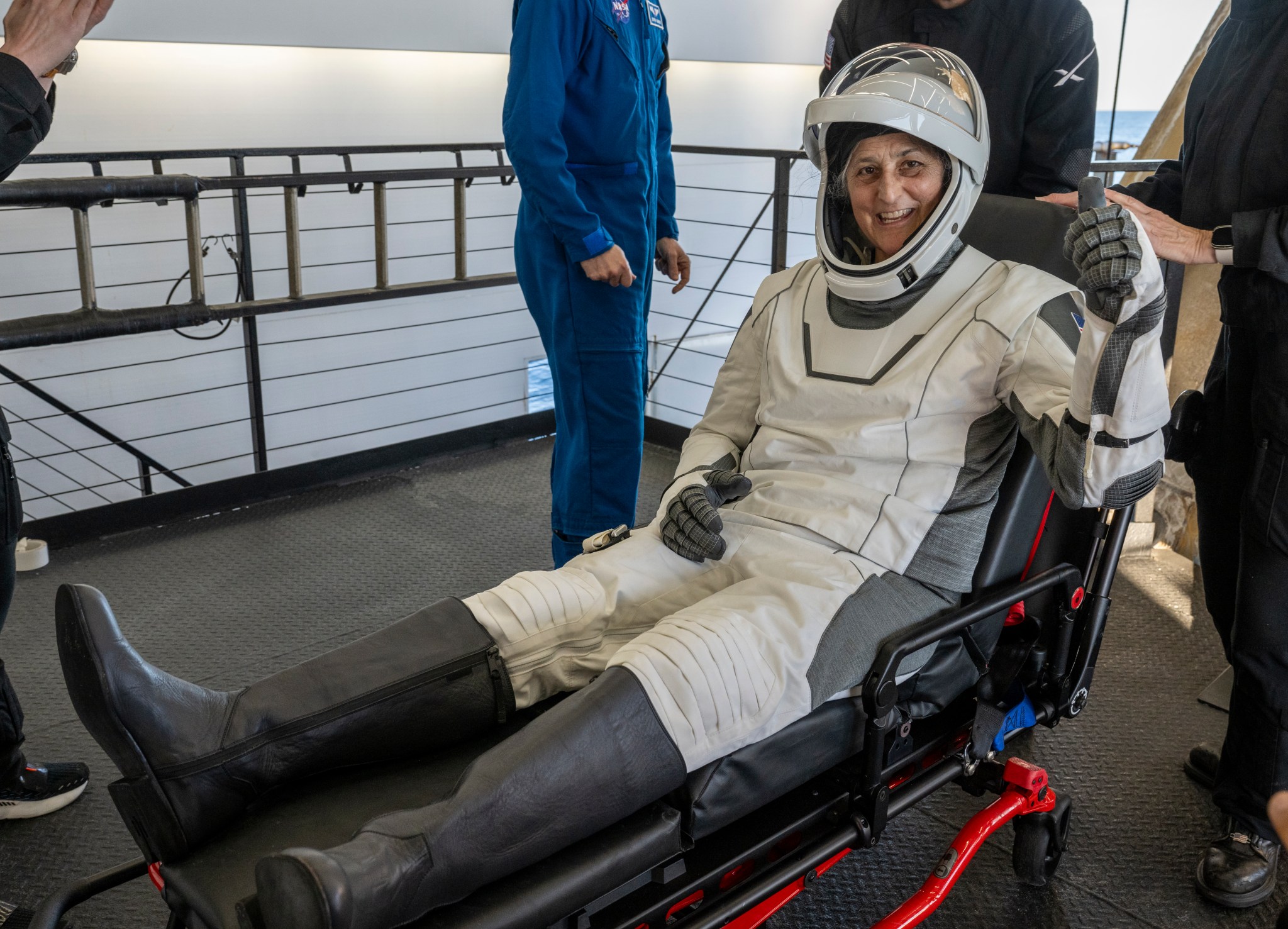 A woman gives a thumbs up in a white spacesuit