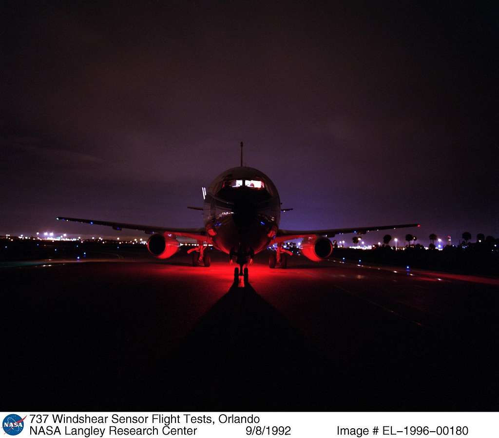 Boeing 737 test aircraft parked on the ramp at night, illuminated by a red ground light beneath the fuselage.