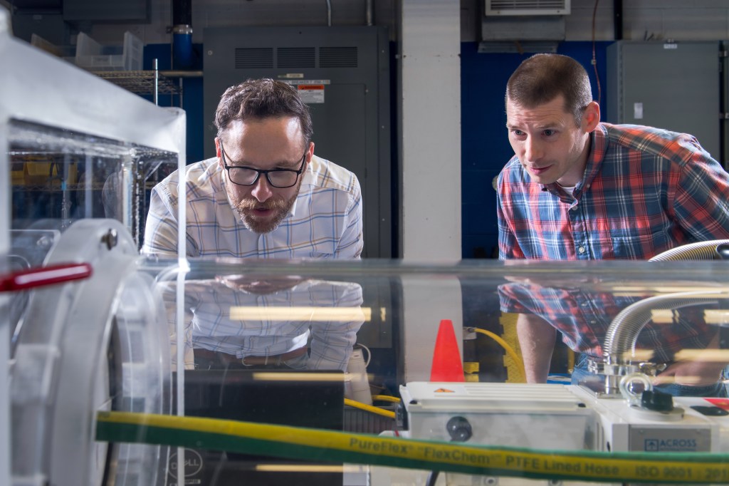 Two men wearing plaid button-down shirts examine testing at the HiACT rig.