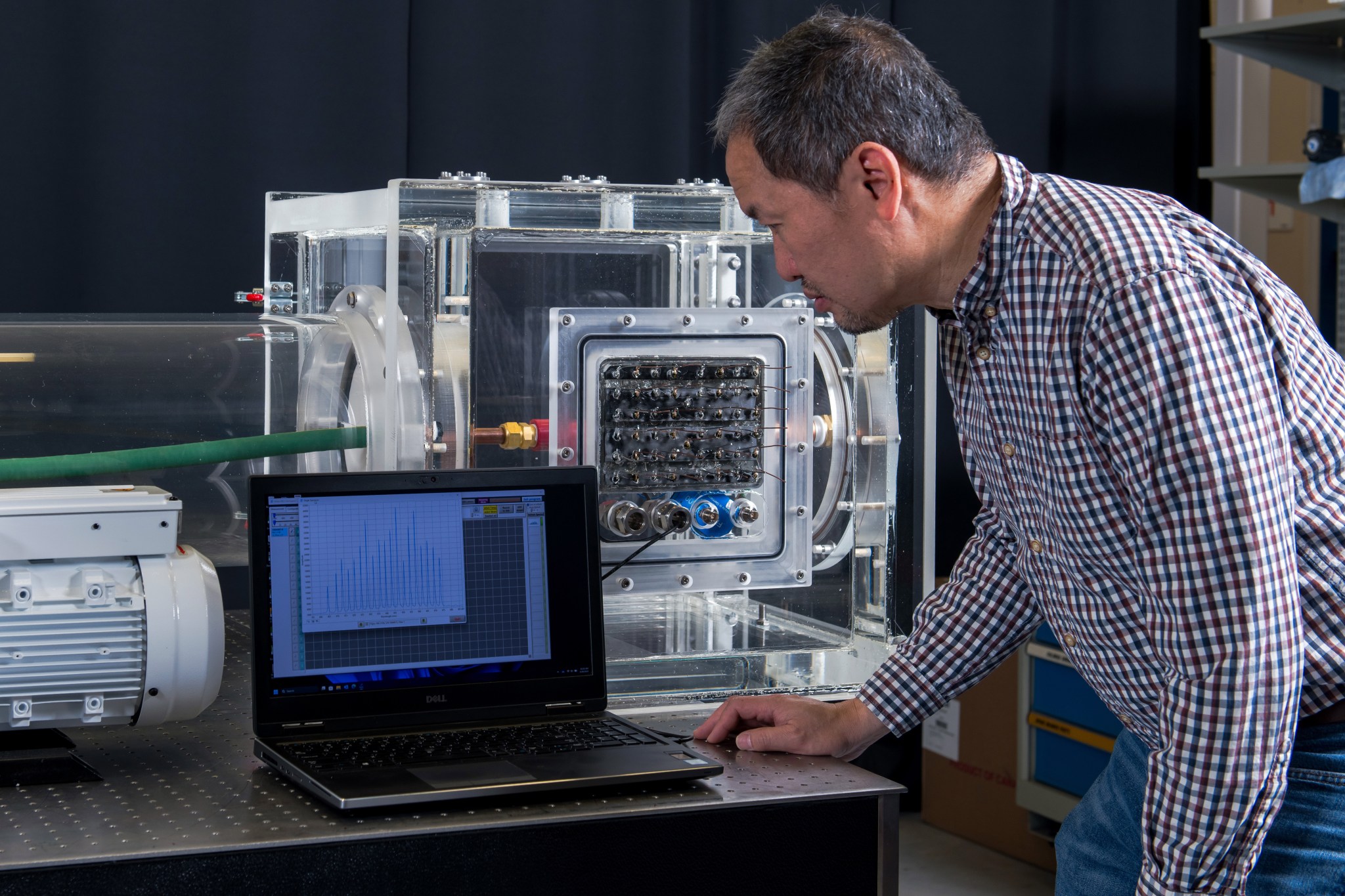 A man standing next to a test rig looks at a laptop with testing data on the screen.