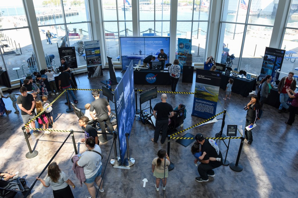 Several hands-on aeronautic-focused activities are set up in a large open area with large glass windows and a view of the lake.