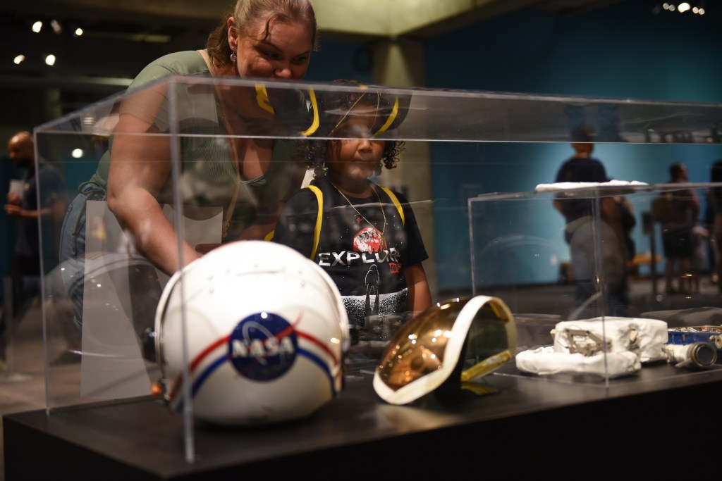 A mother and daughter look inside a clear case that contains a space helmet and other items used by astronauts through the years.
