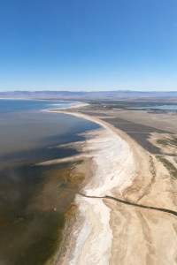 A high view of a lakeshore shows variegated blueish brown water, on a coast with white and tan sand.