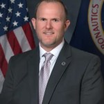 Portrait of Steven Sinacore with American and NASA flags behind him.