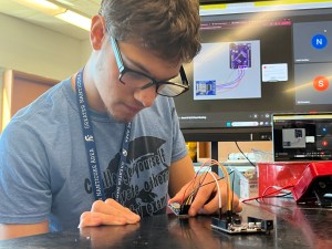 A student stares intently at small device at a workstation.