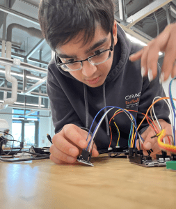 A student studies a small device with multicolored wires extending from it to a circuit board.
