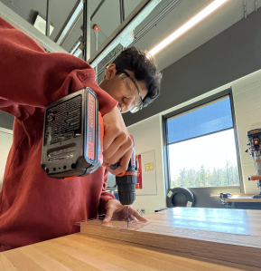 A student uses a drill on a piece of wood.