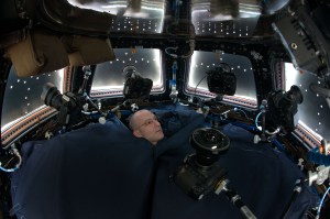 Astronaut Don Pettit is seen in the space station Cupola. Don is surrounded by a dark cloth, and only his head is seen. Five cameras are placed in front of the Cupola windows. The window shutters are partially closed, allowing a small of amount of light to enter the Cupola.