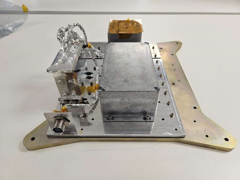 A metal box is mounted on a metal board. Foil covered wires are extending from a smaller mounted box.