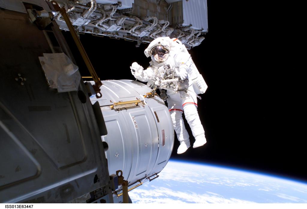 NASA astronaut Jeffrey N. Williams in EMU spacesuit next to an ISS module waves to the camera with the Earth in the lower background.