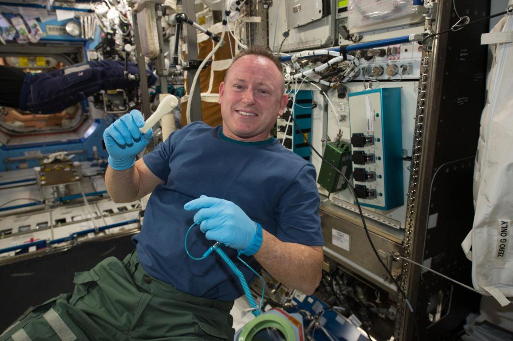 NASA astronaut Butch Wilmore smiles as he holds a 3-D printed ratchet wrench with blue gloves aboard the International Space Station.