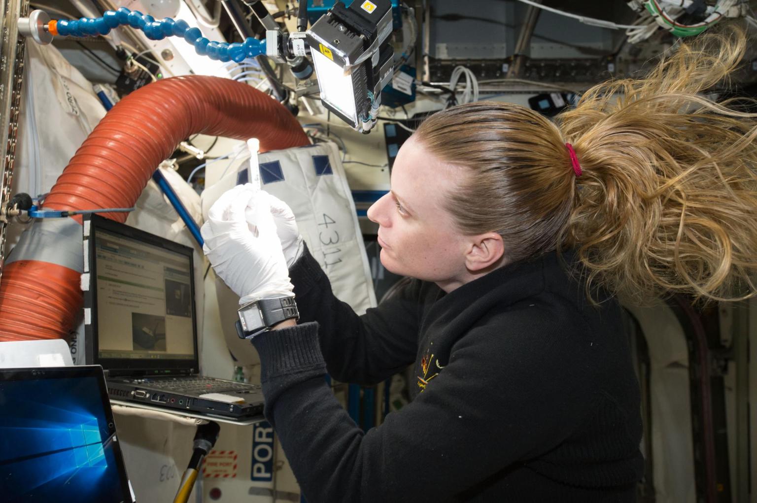 NASA astronaut Kate Rubins is looking towards the left at her hands while working on an experiment on the International Space Station.