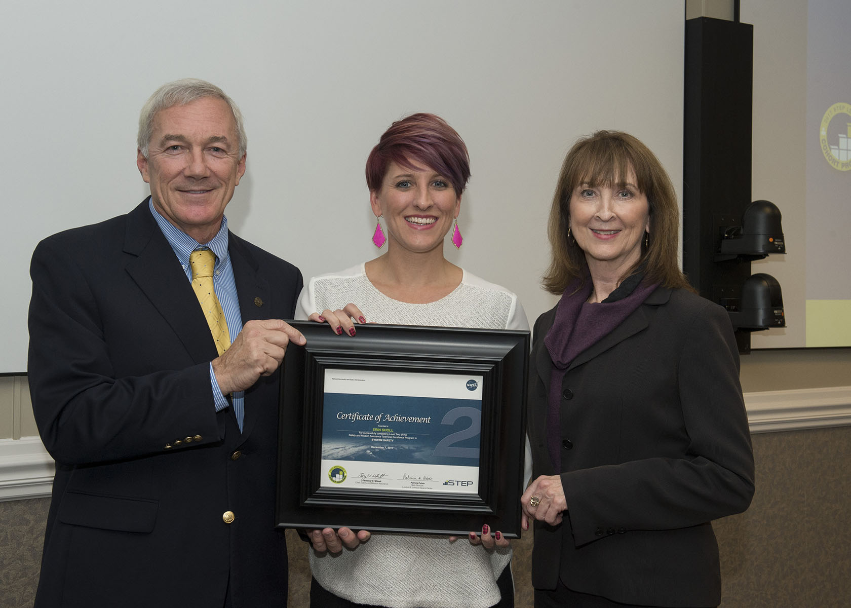 A woman receives a framed honor from two colleagues, a man and a woman.