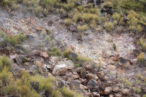 Reddish brown rocks sit on a slope with tufts of green grass. A bit of haze rises from the rocks.