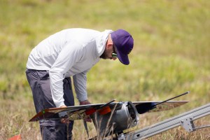 A man in a white longsleeve and purple baseball cap adjusts the wings on a slate-gray device.