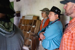 Three men in various hats and long sleeves stand in the right half of the photo, listening to someone out of the frame.