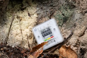 A small white box with a digital screen showing the number 9999 leans against a tan rock.